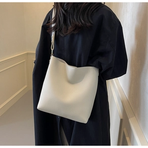 Detail view of cream white lychee leather bucket bag with wide shoulder strap on model