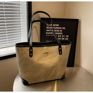 Dettaglio della grande borsa tote in tela beige con manici in pelle nera e borchie