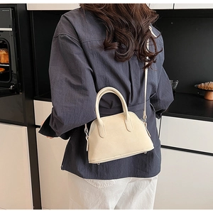 Side view of a beige shell handbag with top handles and adjustable strap in a lifestyle setting