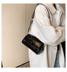 Close-up of black leather cylinder bag with a vintage patterned wide shoulder strap