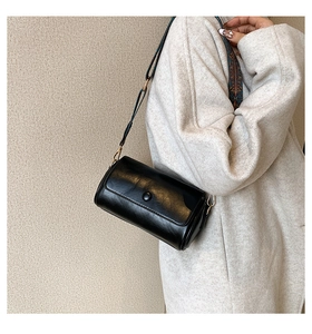 Detail of black cylindrical crossbody bag with vintage patterned wide woven strap on model