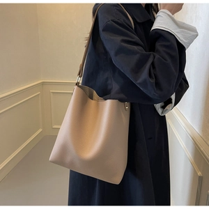 Detailed view of beige lychee texture leather bucket bag on a navy trench coat