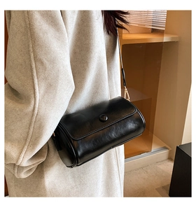 Detailed side view of a black cylindrical crossbody bag with gold hooks and leather texture
