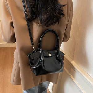Détail d'un sac cabas en cuir verni noir brillant avec poignées rondes et accents métal