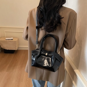 Gros plan d'un sac plissé noir brillant porté à l'épaule dans un style minimaliste