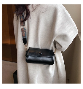 Detail of black cylinder shoulder bag with colorful bohemian embroidered wide strap