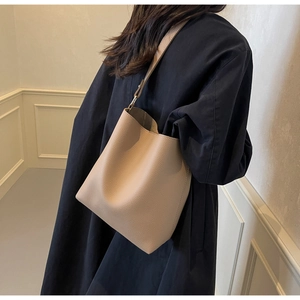 Close-up of beige lychee grain leather bucket bag worn by model on dark navy coat