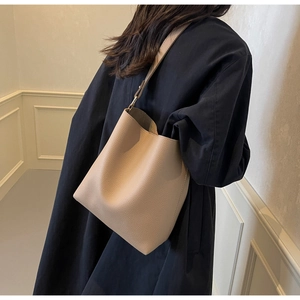 Detail view of beige lychee grain leather bucket bag on model's shoulder in black coat