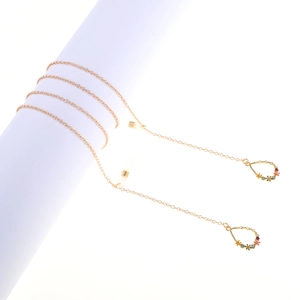 Golden eyewear chain with colorful floral charms and teardrop pendants on white stand