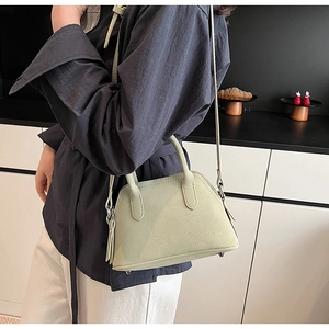 Detail of light green shell bag in grainy faux leather with crossbody strap and studs