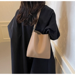 Side view of model wearing a light brown pebbled leather bucket bag with shoulder strap