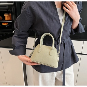 Detail view of sage green shell-shaped bag with lychee texture and sturdy handles