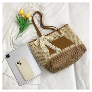 Detail of woven straw tote bag featuring contrast leather trim and white lace bow