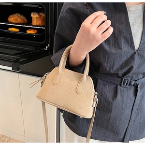 Close-up of beige shell bag with lychee texture and long tassel zipper detail