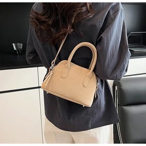 Close-up of beige pebble grain leather shell bag worn by model in a minimalist setting