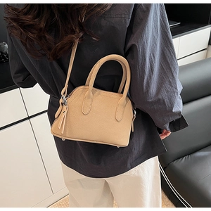 Detail of a beige shell-shaped crossbody bag featuring lychee texture and tassel charm