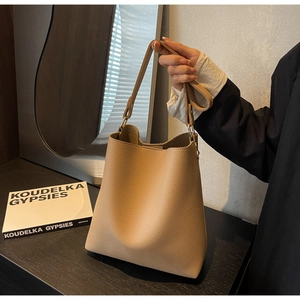 Close-up of warm camel leather bucket bag featuring elegant lychee grain texture and gold hardware