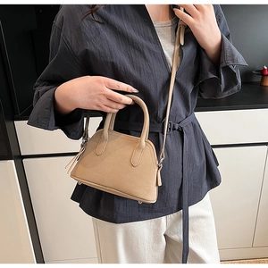 Elegant beige shell-shaped bag with tassel detail worn as a crossbody on person
