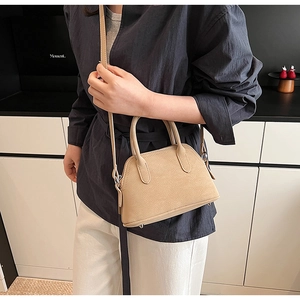 Detail view of a beige pebble leather shell bag with adjustable strap and metal studs