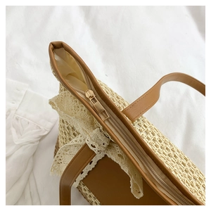 Detail of hand-woven straw bag featuring delicate lace trim and a secure gold metal zipper
