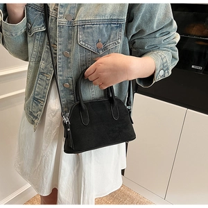 Detail of a black matte mini shell bag showing handle and shoulder strap on a model