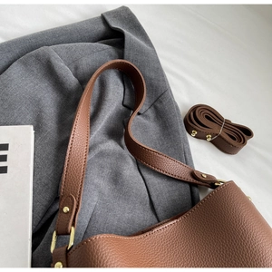 Detail of brown litchi textured tote bag with gold rivets on grey blazer background