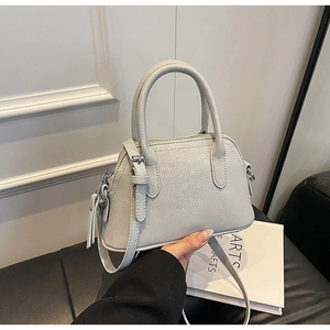 Detail of light grey shell crossbody bag featuring pebble leather texture and metal buckle