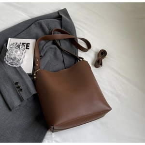 Detail of brown lychee grain leather bucket bag with adjustable straps on a blazer