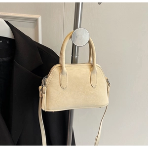 Detail of cream crossbody bag featuring litchi grain texture and silver metal hardware