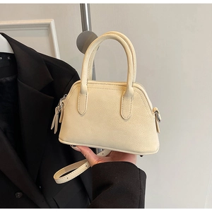 Detail of cream mini shell bag with pebble grain texture and silver hardware details