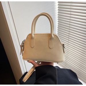Detail of beige lychee textured leather bag with round handles and adjustable strap