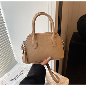 Detail of a beige lychee pattern handbag held by hand with an adjustable shoulder strap