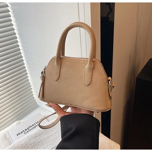 Detail of beige pebble leather shell bag with silver hardware and sturdy dual handles