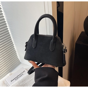 Detail of a black shell-shaped handbag with matte texture and silver zipper hardware