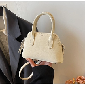 Mini cream shell bag held by hand, featuring lychee grain texture and silver hardware