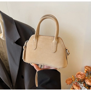 Close-up of beige pebble grain leather shell bag with top handles and gold-tone zipper