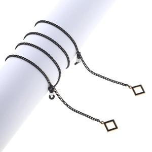 Sleek black eyewear chain with golden square pendants on a white display pedestal