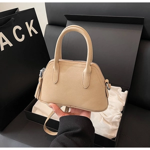 Detailed close-up of beige shell bag featuring pebble leather texture and silver hardware