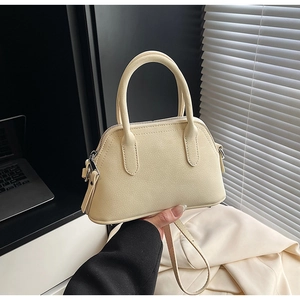 Detail of cream crossbody bag in litchi textured leather held by a model in soft light