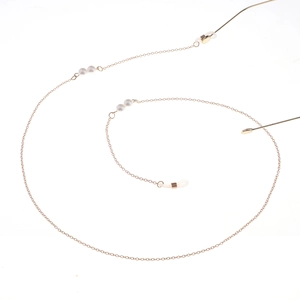 Détail d'une fine chaîne de lunettes dorée avec perles et connecteurs en silicone transparent