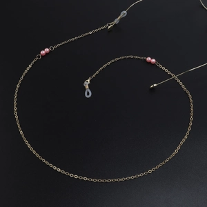 Elegant gold metal eyewear chain featuring delicate pink pearls on a sleek black background
