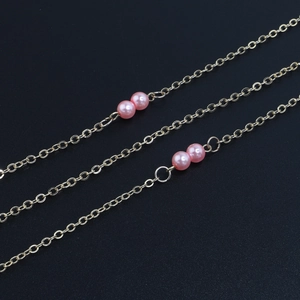 Close-up of golden metal glasses chain with elegant pink pearls on black background