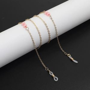 Detail of gold eyewear chain with pink pearls on a white cylinder over black background