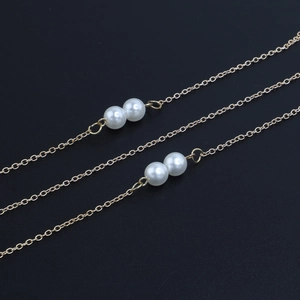 Chaîne à maillons dorés minimaliste avec deux perles blanches rondes sur fond noir