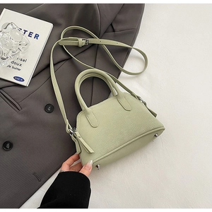 Detail view of mint green handbag featuring textured leather, top handles and metal feet