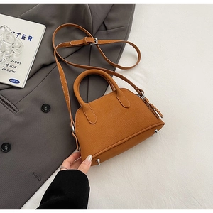 Close-up of brown lychee leather shell bag with silver feet on a grey blazer
