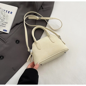 Detail view of cream-colored shell bag featuring metal zippers and dual sturdy top handles
