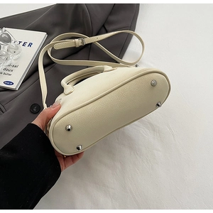 Detailed macro view of beige faux leather handbag featuring metal bottom rivets and strap