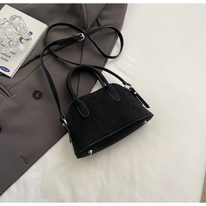 Detail of black suede shell bag featuring silver metal feet and adjustable crossbody strap