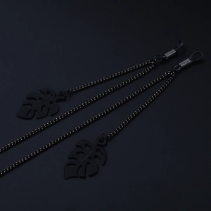 Matte black glasses chain featuring hollow monstera leaf pendants on a black background